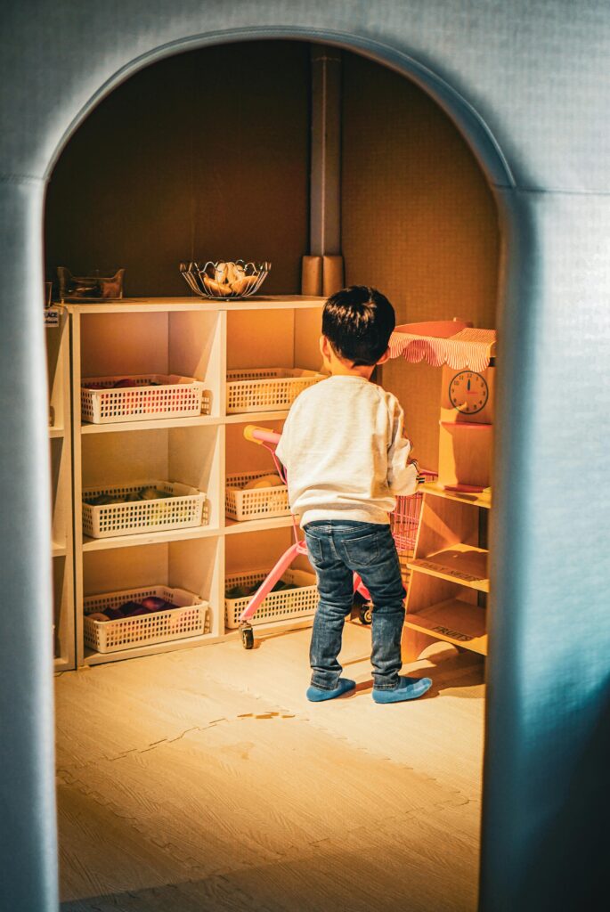 A young child with black hair playing indoors surrounded by shelves and toys.