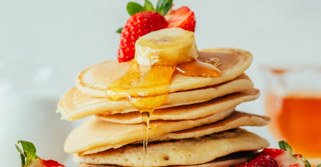 Stack of fluffy pancakes with strawberries, banana slices, and honey. Perfect breakfast treat.