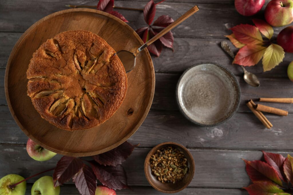 A homemade apple cake surrounded by autumn leaves and spices, top view.