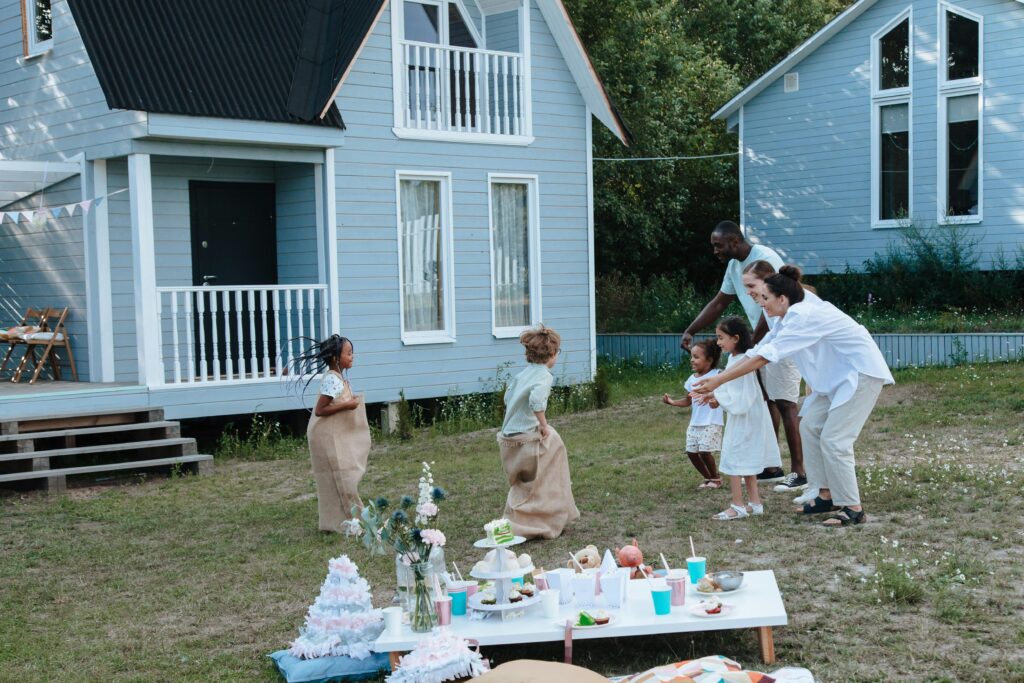 Children enjoying a sack race with parents cheering in a backyard garden.