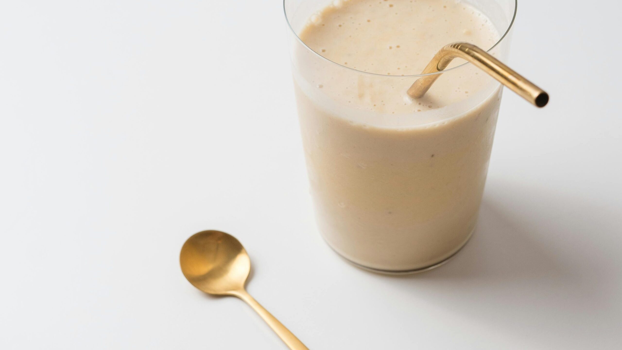 A minimalist shot of an almond milkshake with golden accents on a white background.