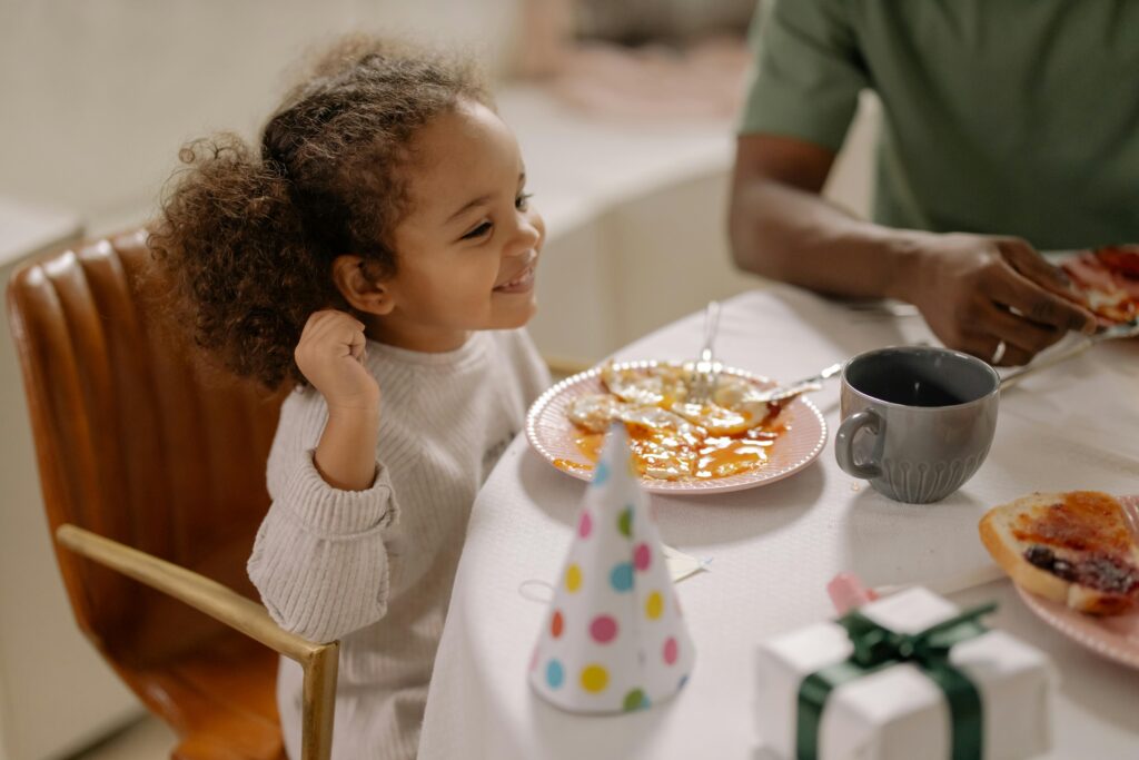 Smiling child with curly hair enjoying breakfast with family, celebrating indoors.