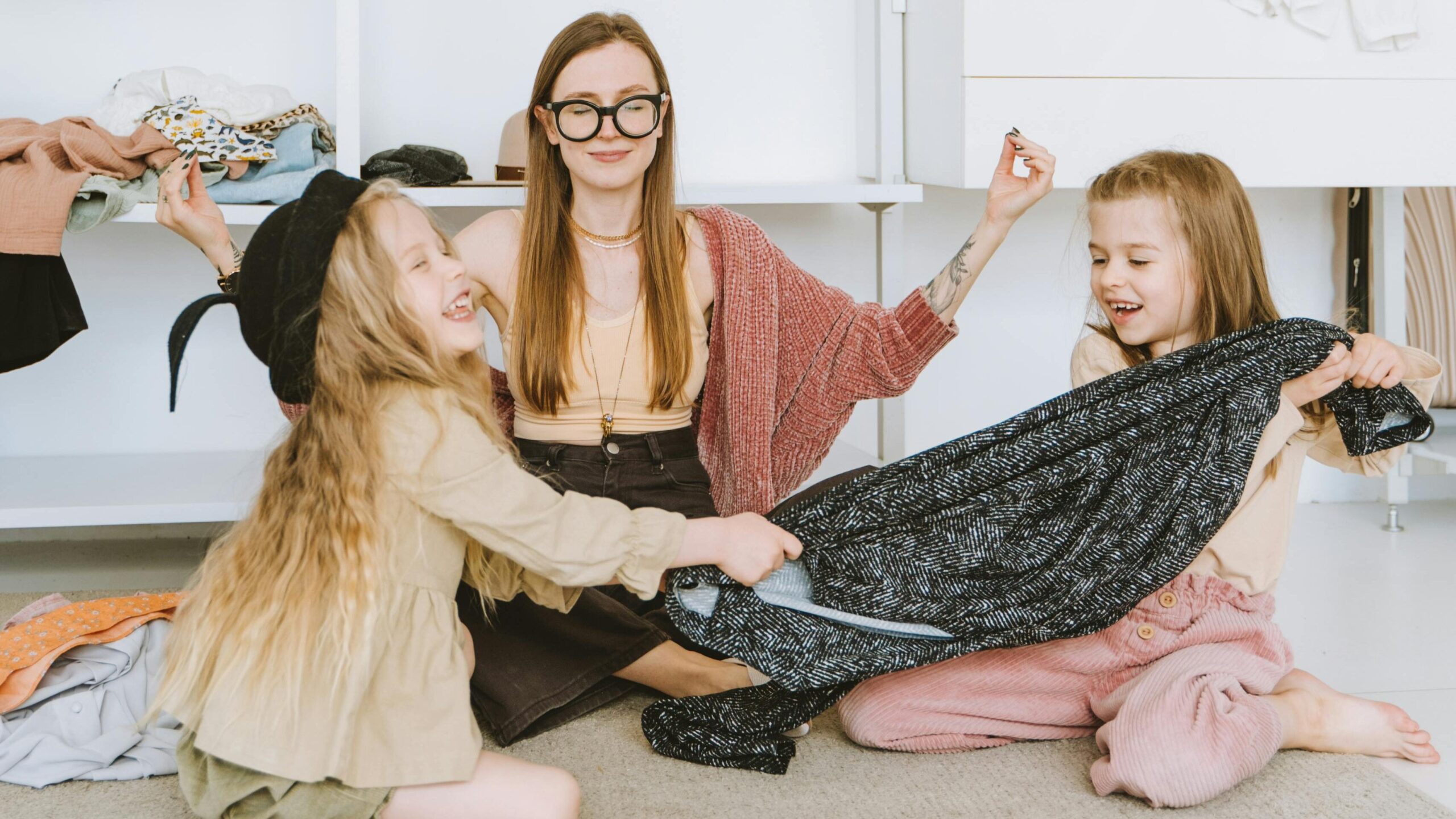Mother and daughters bonding while playing with clothes in a modern wardrobe room.